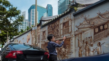 ผู้หญิงคนหนึ่งกำลังถ่ายรูปภาพวาดบนฝาผนัง Thian Hock Keng ตามถนน Amoy